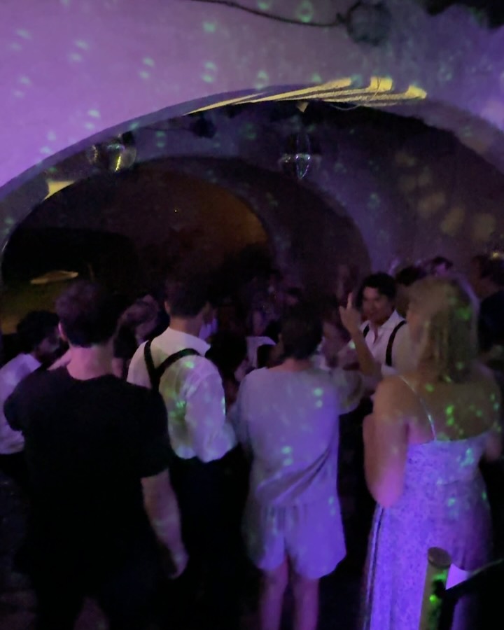 Guests dancing in a vaulted stone room under purple disco lighting